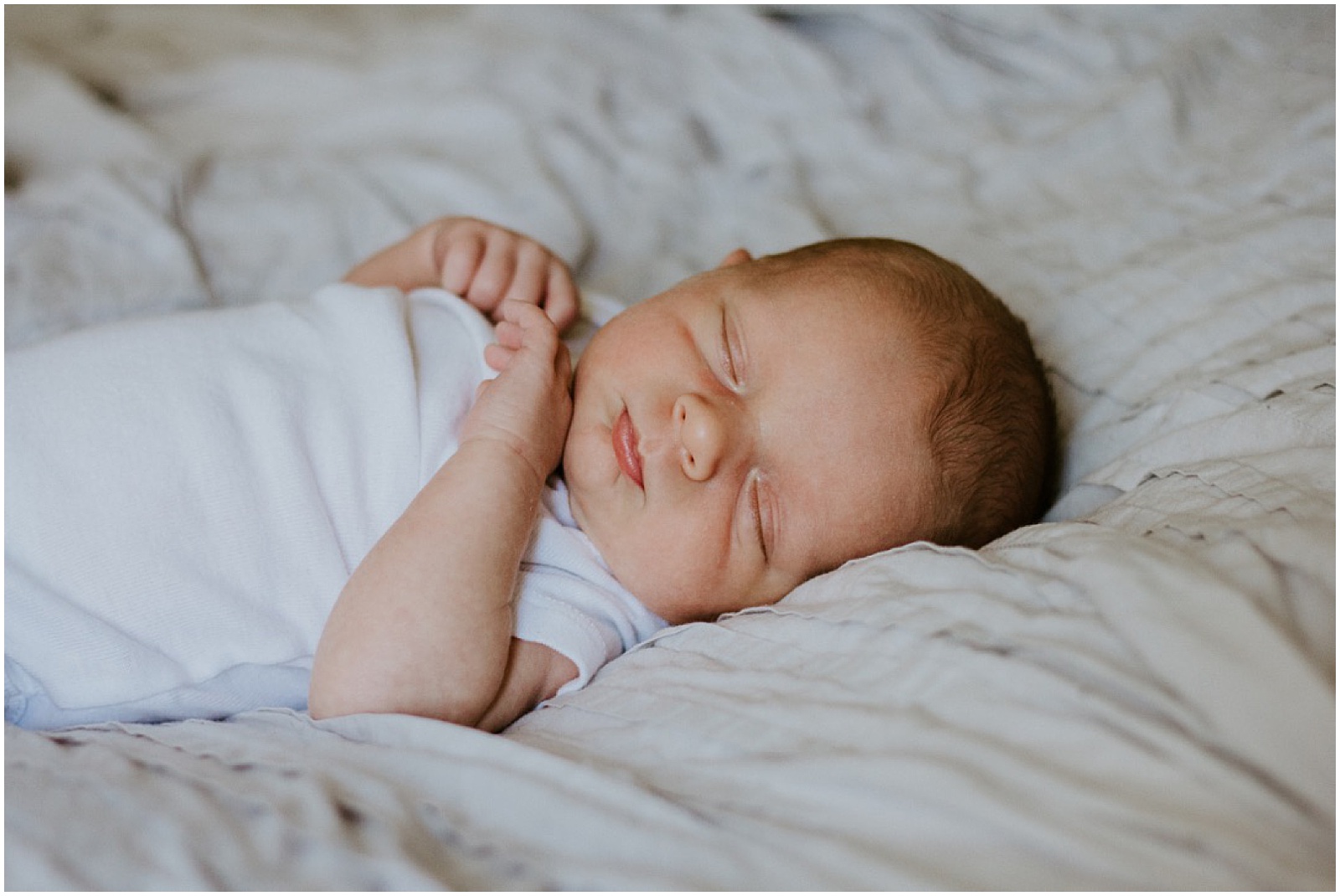 A baby sleeps on a bed during a newborn photo shoot.
