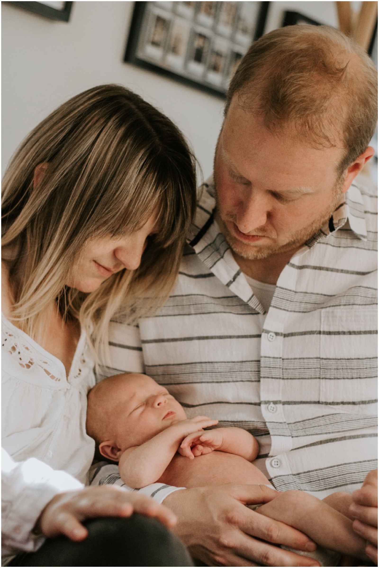 A mother and father cuddle a newborn on a couch for a memory book photo.