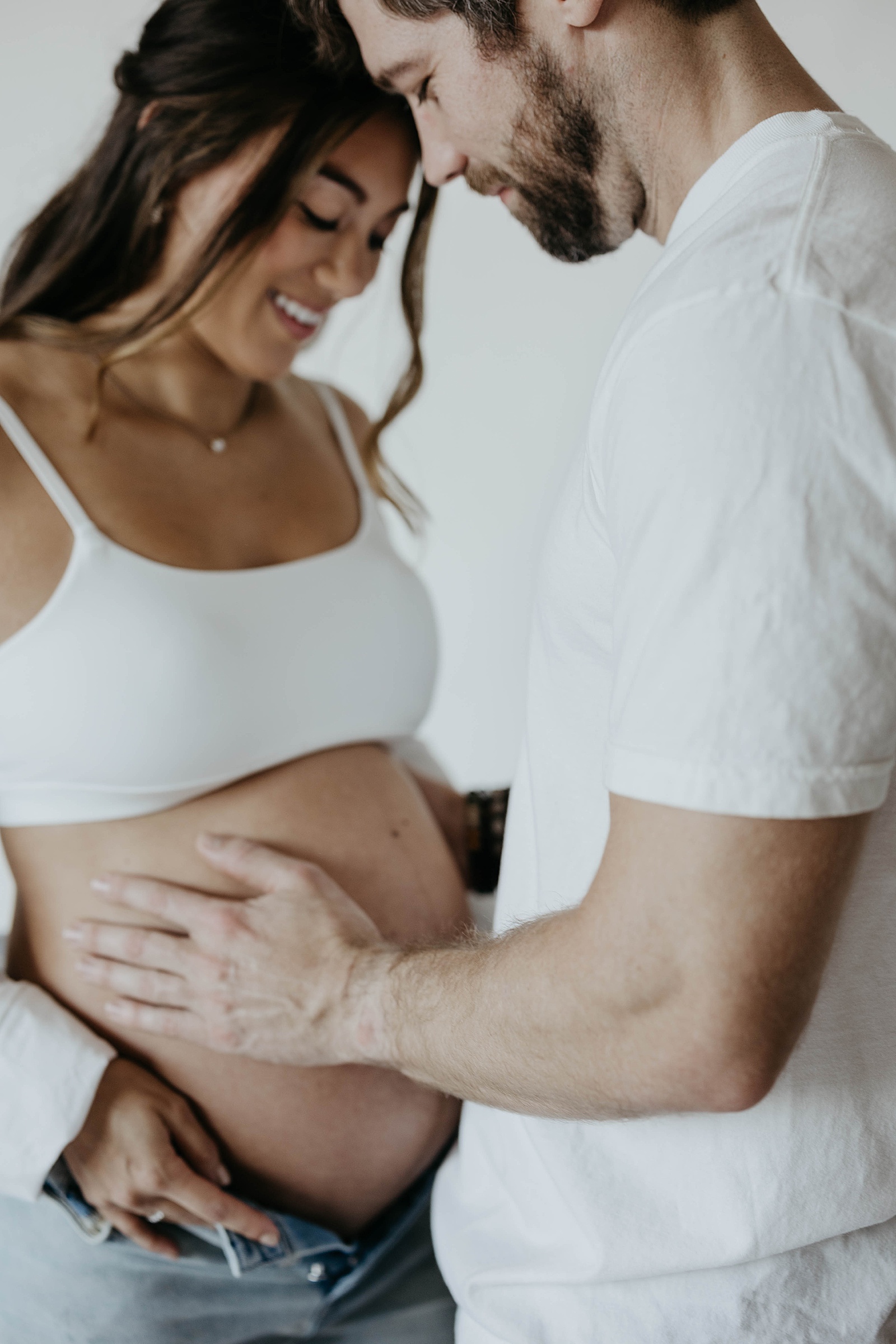 A man places his hand on his wife's baby bump in a studio maternity photoshoot.