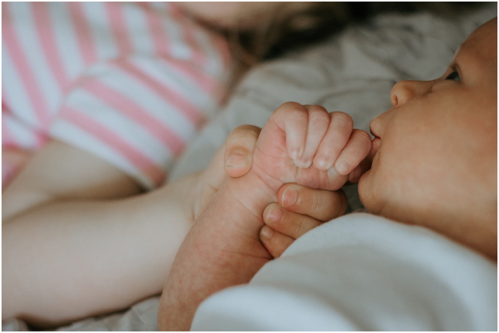 A toddler holds a baby's hand.