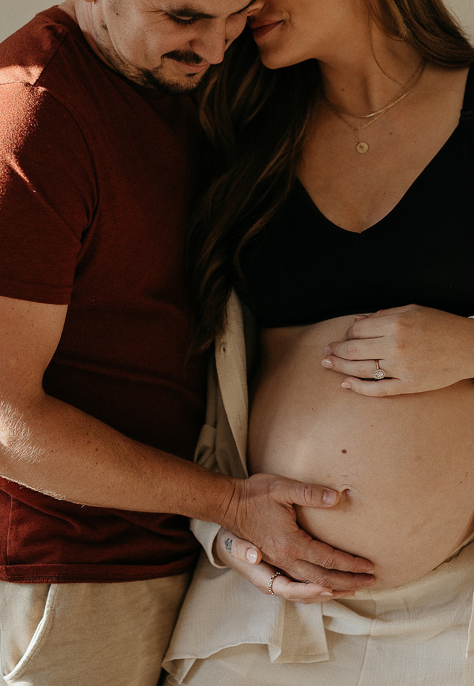 A man puts his hand on his wife's baby bump in a maternity photoshoot.