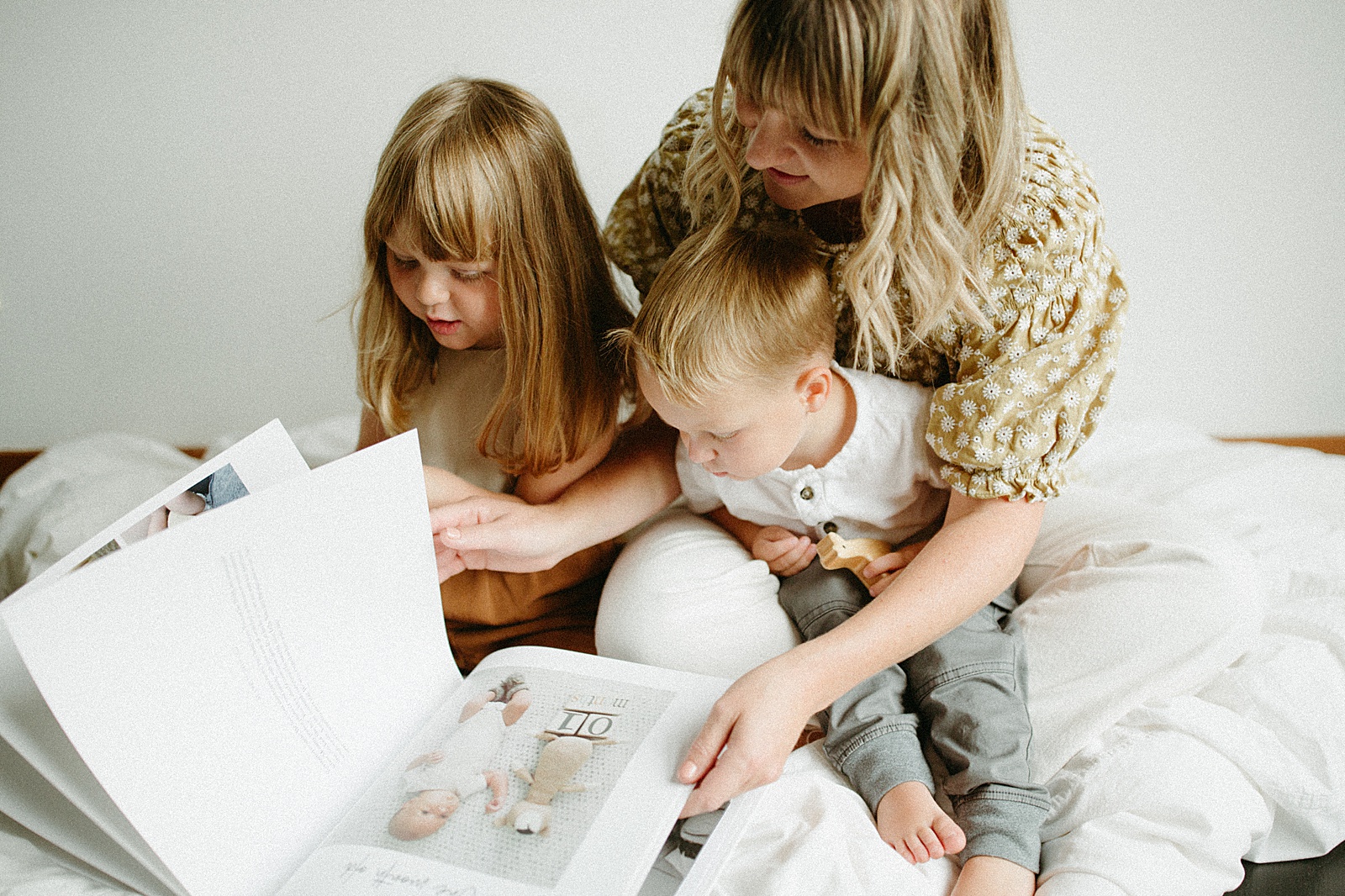 A mom holds two children in her lap as they flip through a custom photo album.