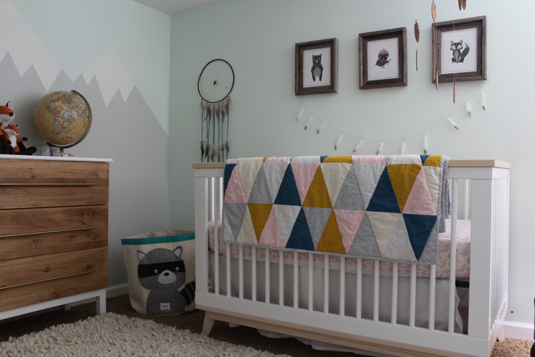 A quilt drapes over the edge of a crib in a room decorated with woodland nursery decor ideas.