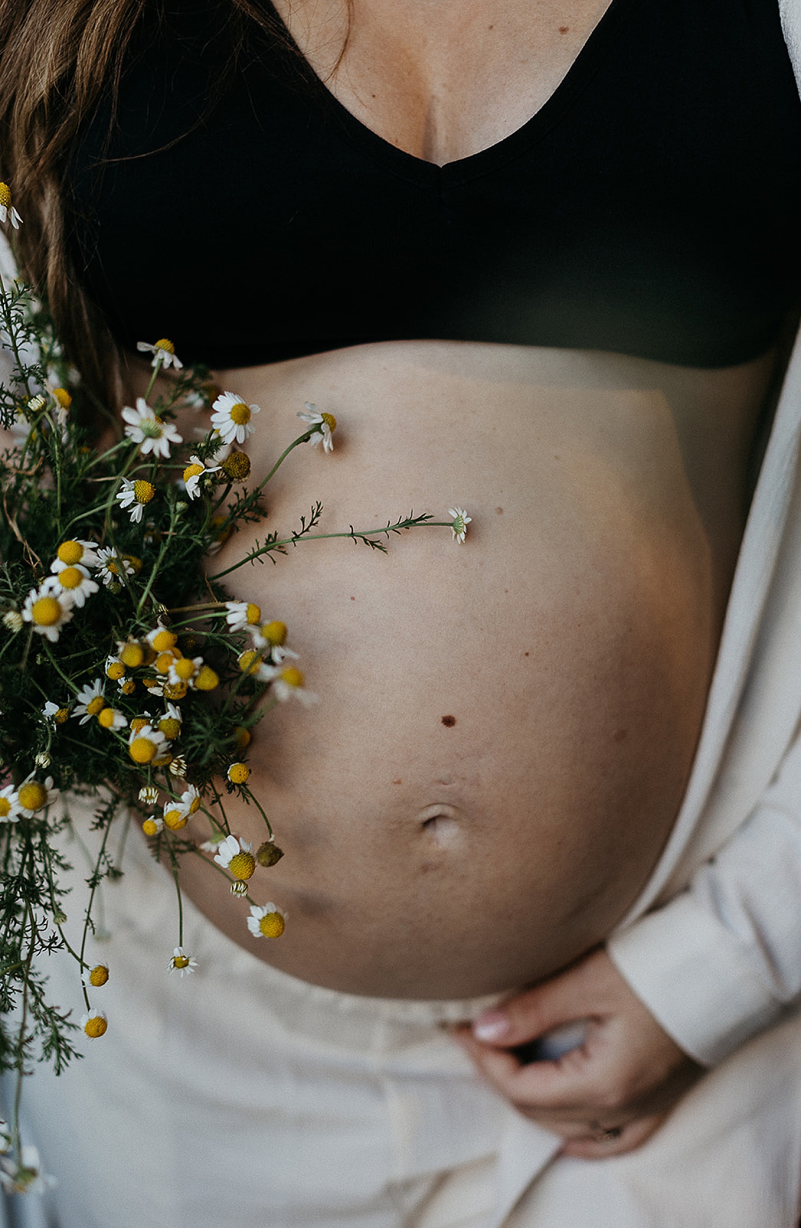A pregnant woman holds a bouquet of flowers next to her baby bump for a maternity photoshoot.