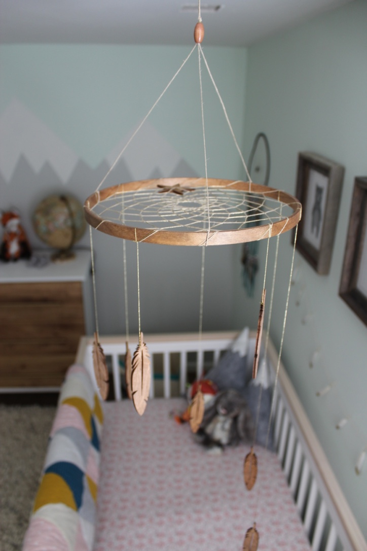 A handmade dream catcher mobile hangs over a crib in a forest themed nursery.