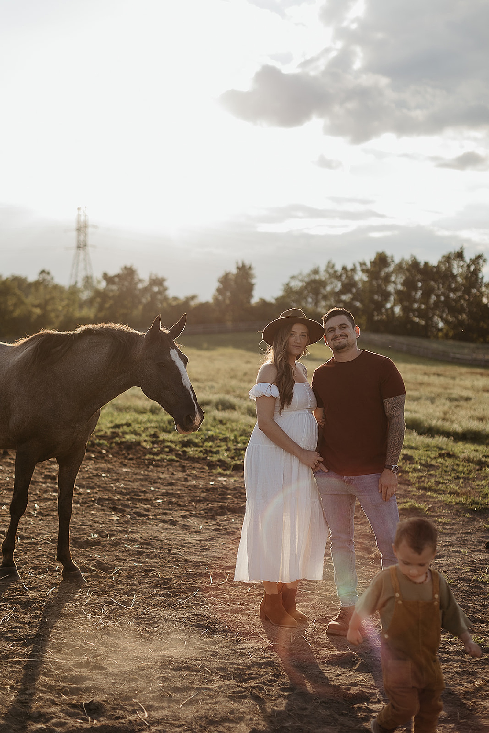 A family of three poses beside a horse in a maternity photoshoot.