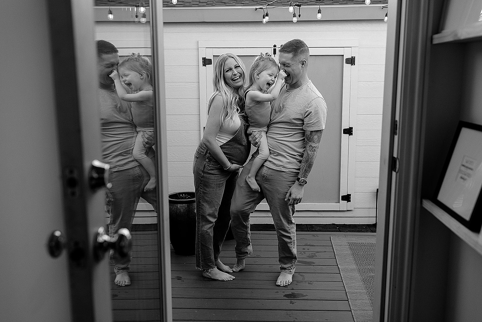 A pregnant mother and father hold a toddler during a maternity photoshoot at home.