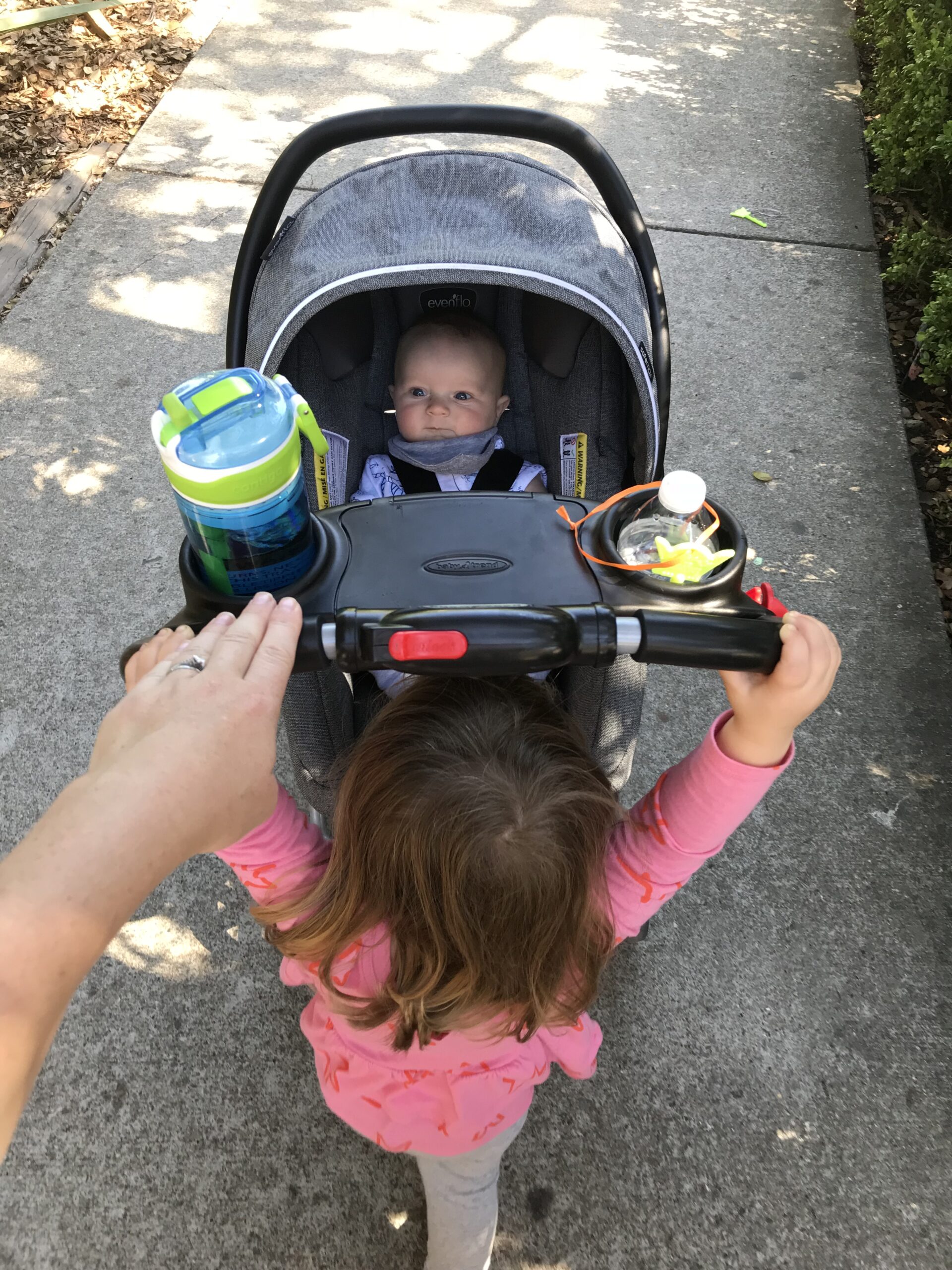 A toddler pushes a baby in a stroller.
