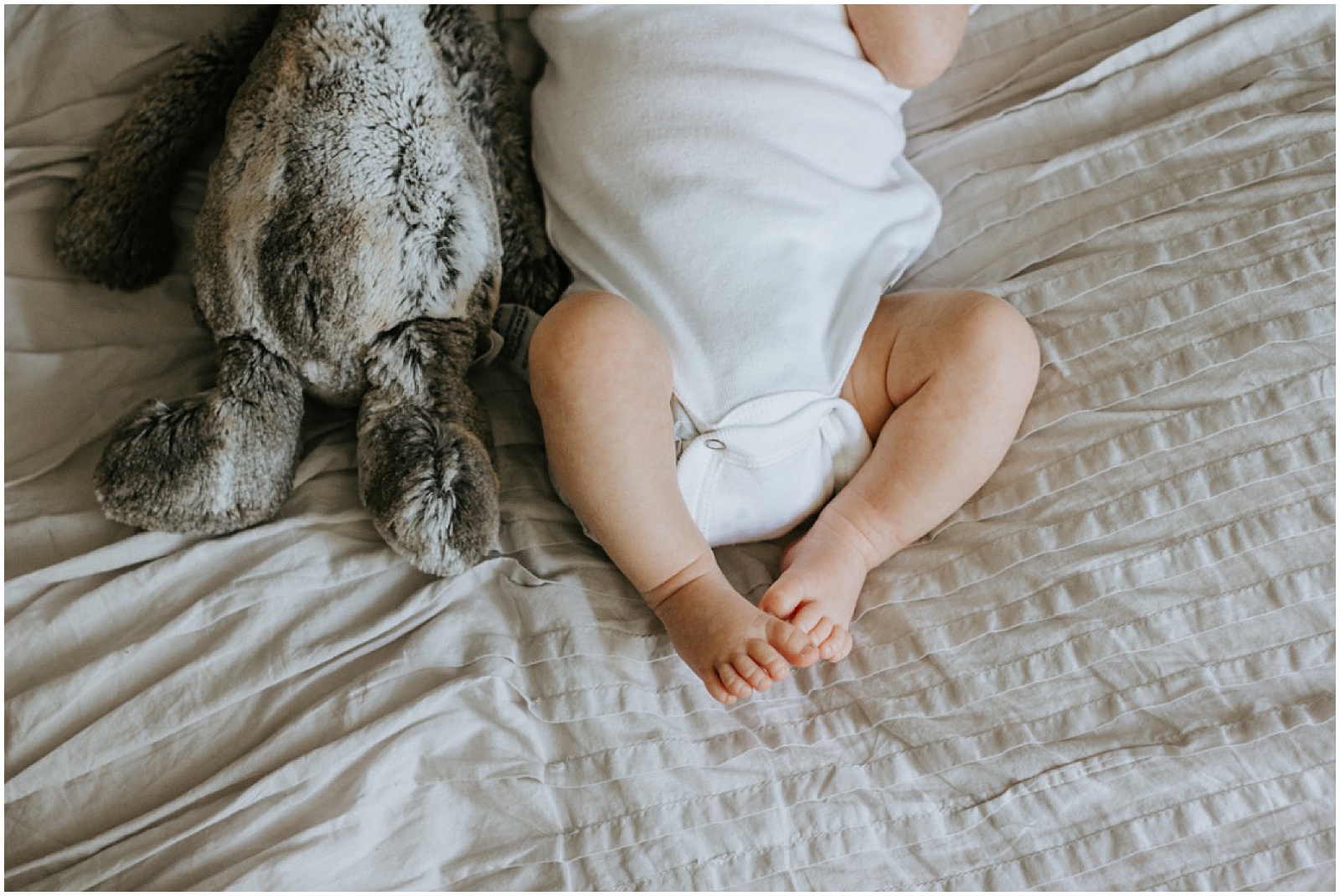 A newborn baby lies beside a stuffed animal.