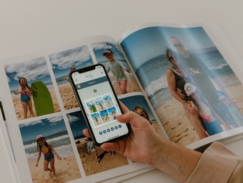 A woman holds her phone open to a photo book maker app in front of a family photo album.
