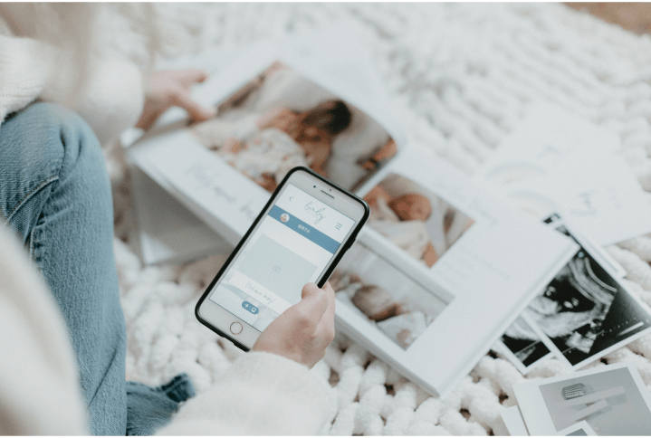 Hand holding a mobile phone showing baby book app screen and keepsake baby book